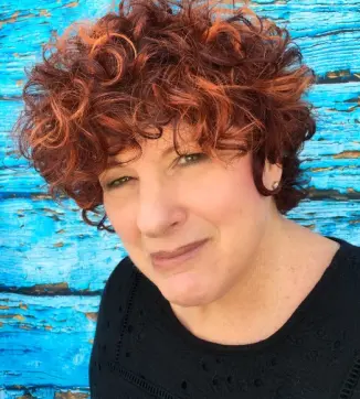 Investigative services professional with curly auburn hair and a black top against a blue wooden wall.